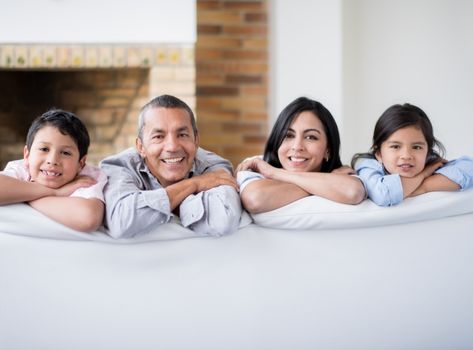 Photo d'une famille assise dans le canapé et qui regarde derrière en souriant à pleine dents