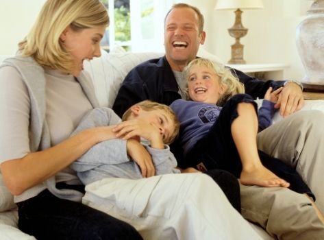 Famille complice qui rie aux éclats assise sur le canapé